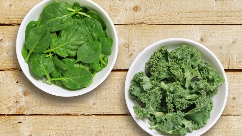 Overview of bowls of spinach and kale on a wooden table