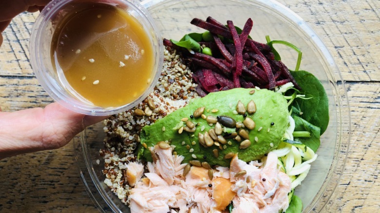 Hand pouring salad dressing out of container onto salad