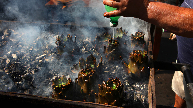 Person cooking artichokes on a charcoal grill