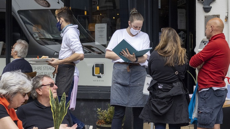 Server taking a reservation at outdoor restaurant wearing mask