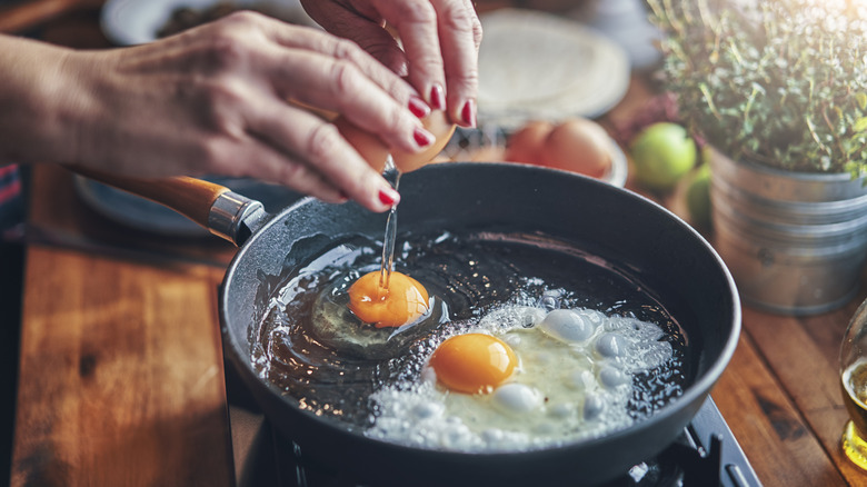 Hands with red nails cracking egg into hot pan