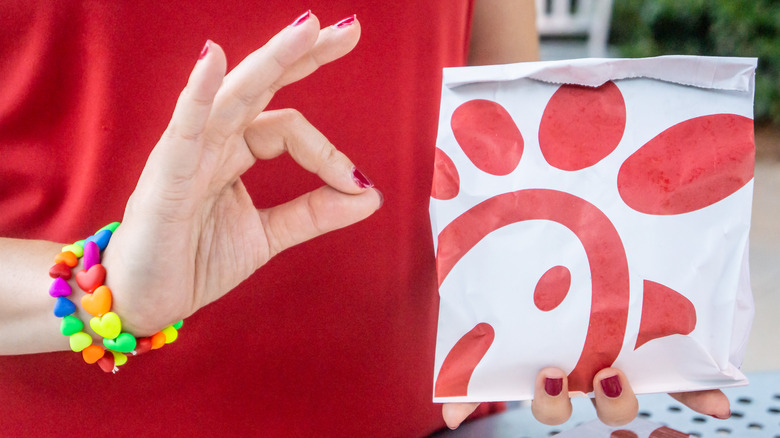 Person holding up "OK" sign language next to bagged Chick-fil-A chicken sandwich