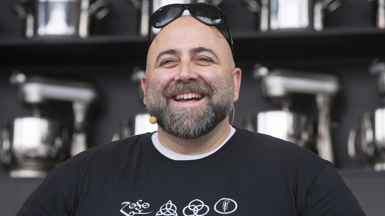 Duff Goldman smiles in an orange T-shirt and gray hat