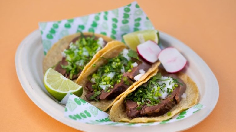 Three tacos on a plate with peach background