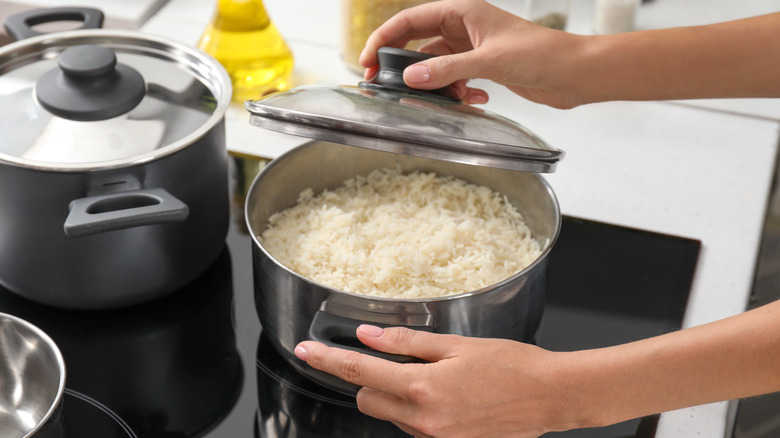 person lifting lid on rice in a pot on stove