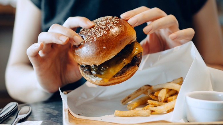 Person's hands holding burger with fries