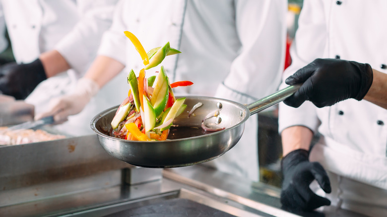 Black-gloved chef sauteing vegetables