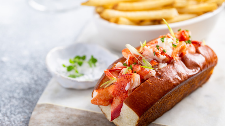 A lobster roll garnished with herbs and french fries in the background