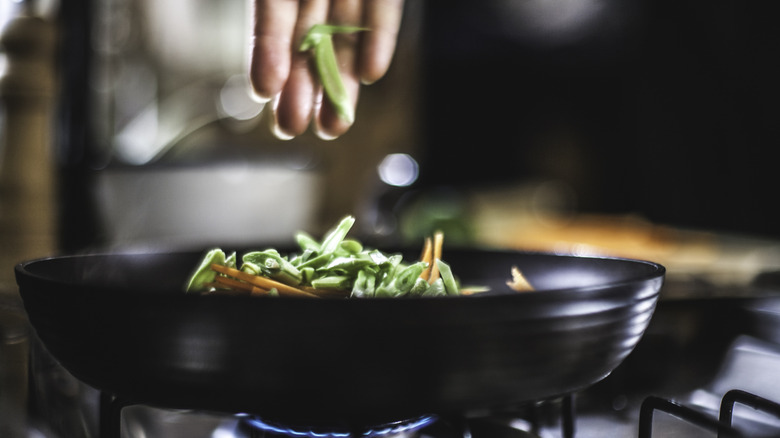 hand putting green beans in pan