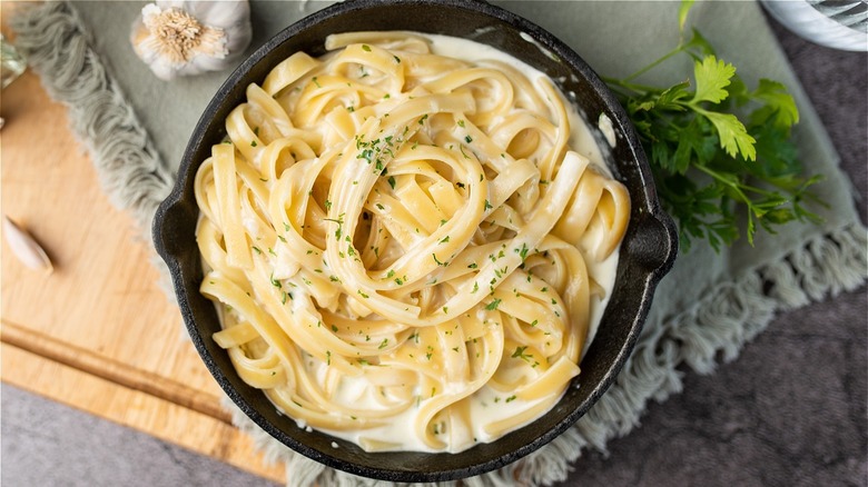 Fettuccine Alfredo dish topped with herbs in cast iron dish