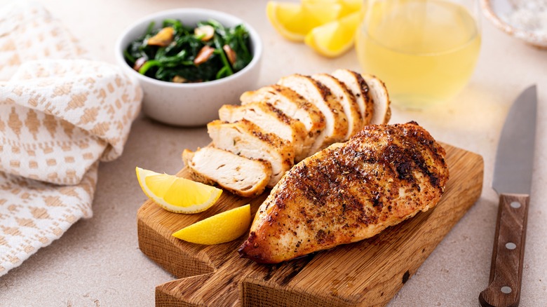 sliced cooked chicken breast with lemon wedges on board