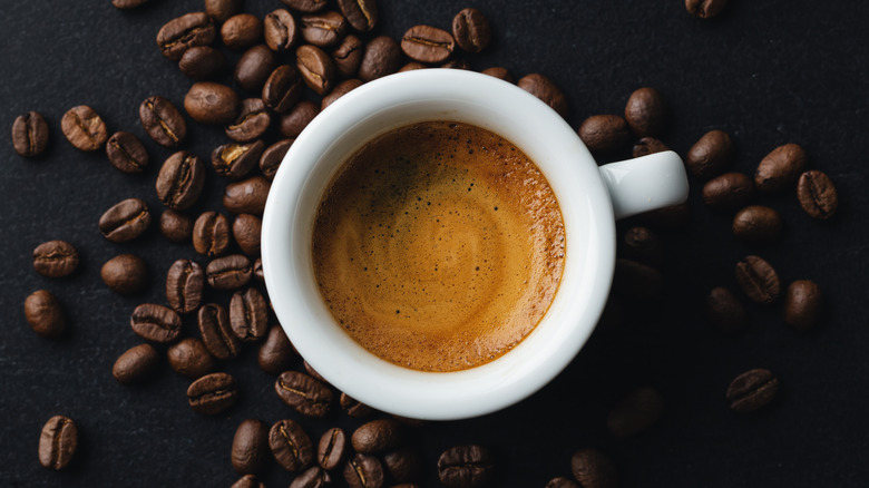 A shot of espresso around coffee beans in a black background 