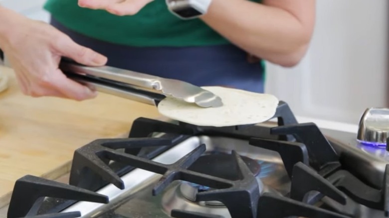 tongs holding tortilla over stove