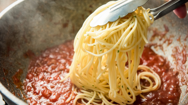 pasta being added to pan of sauce