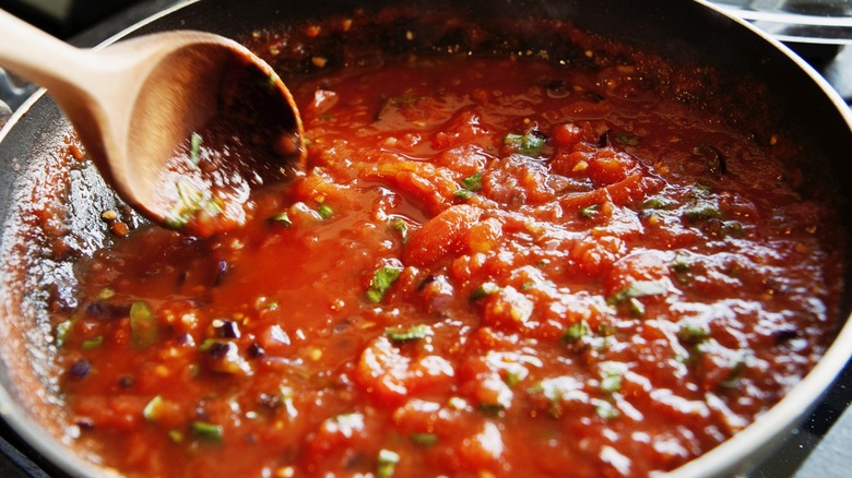 Red sauce cooking in pan with wooden spoon