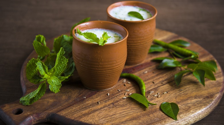 Two glasses filled with frothy white liquid topped with mint and surrounded by mint