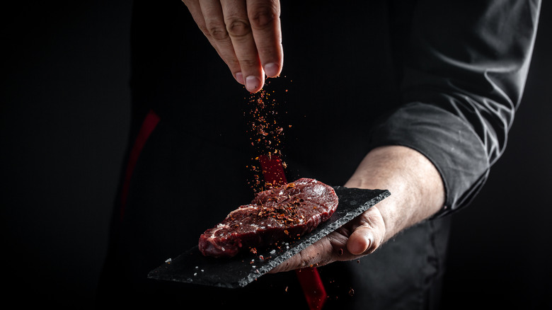 A steak being seasoned by hand