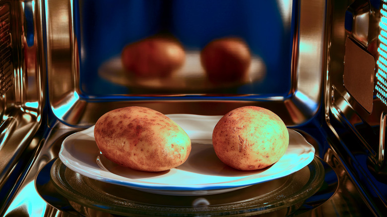 two potatoes on plate in microwave