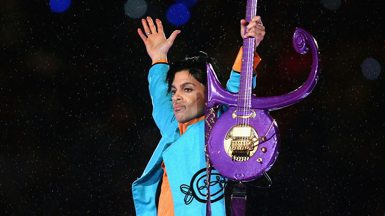 Prince holding up his purple guitar on stage