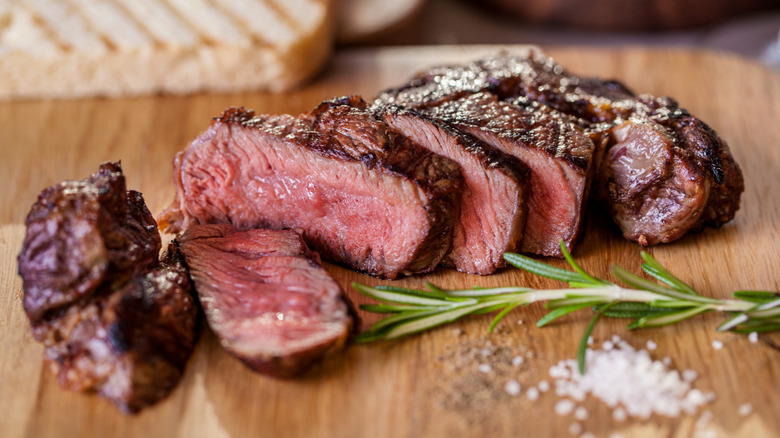 lean cut of cooked serloin steak on wood board with herbs