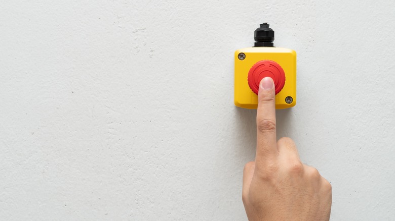 Person's hand pressing red emergency button