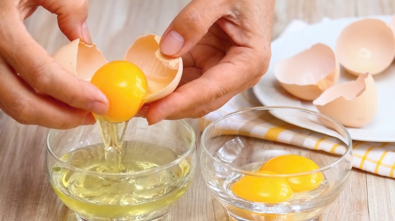 Hands separating white and yolk of cracked egg