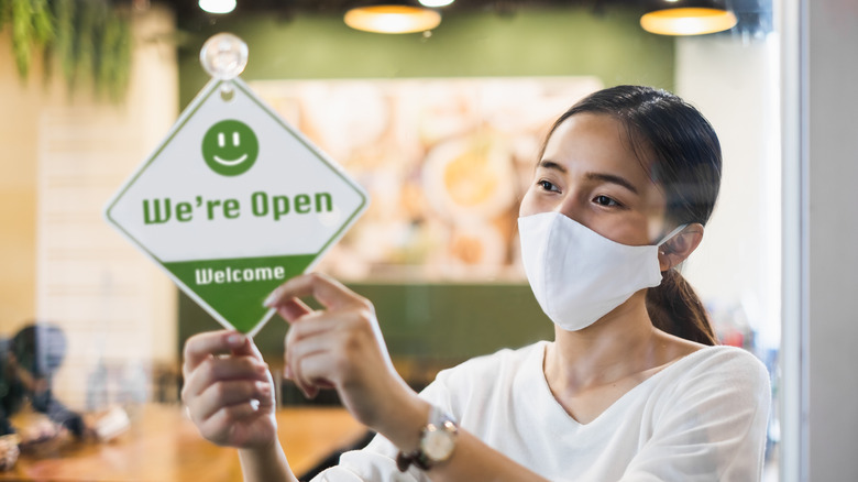 A person flipping a green open sign