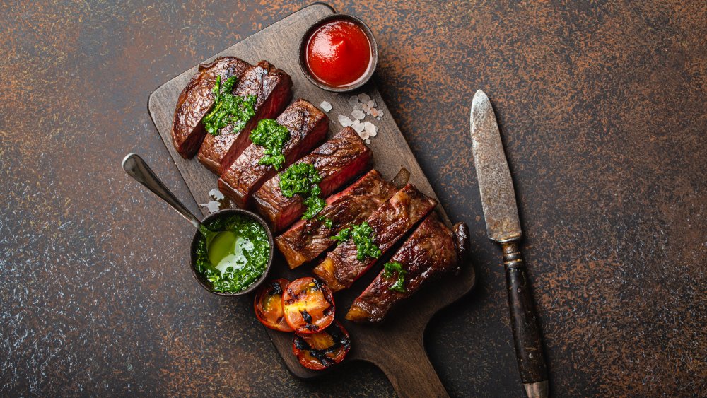 Steak topped with chimichurri sauce and a side of tomatoes and ketchup