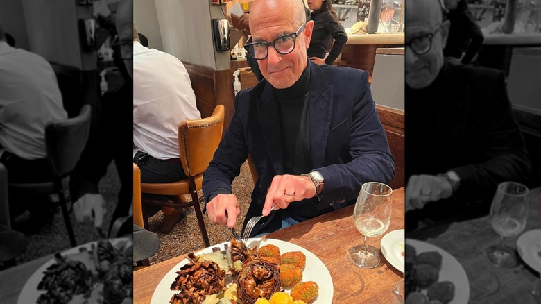 Stanley Tucci cutting into a plate of Italian food at a restaurant