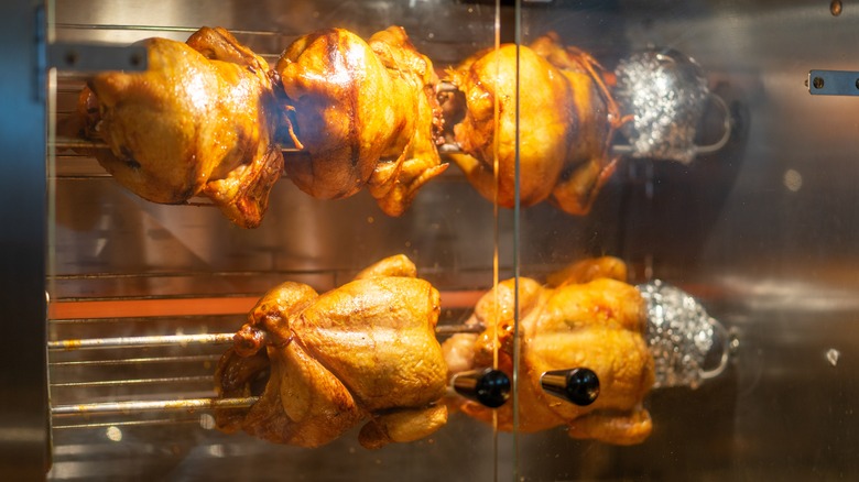 rotisserie chickens on a spit behind oven doors