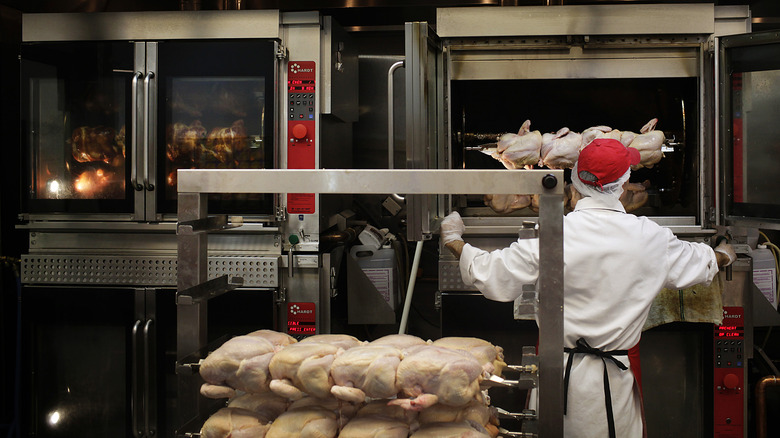 store worker loading a rotisserie with raw chickens