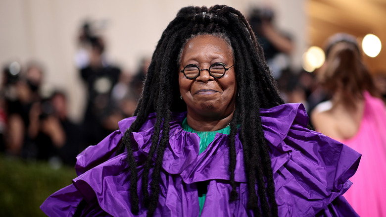 Whoopi Goldberg wears a purple dress and glasses