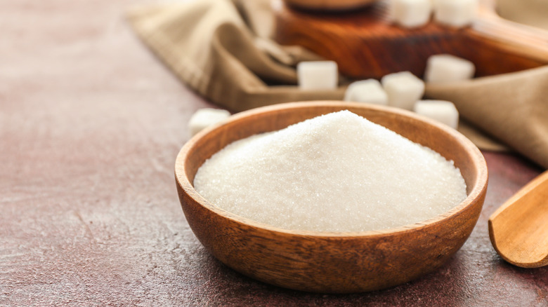 A bowl of sugar in a wooden bowl with sugar cubes int he background