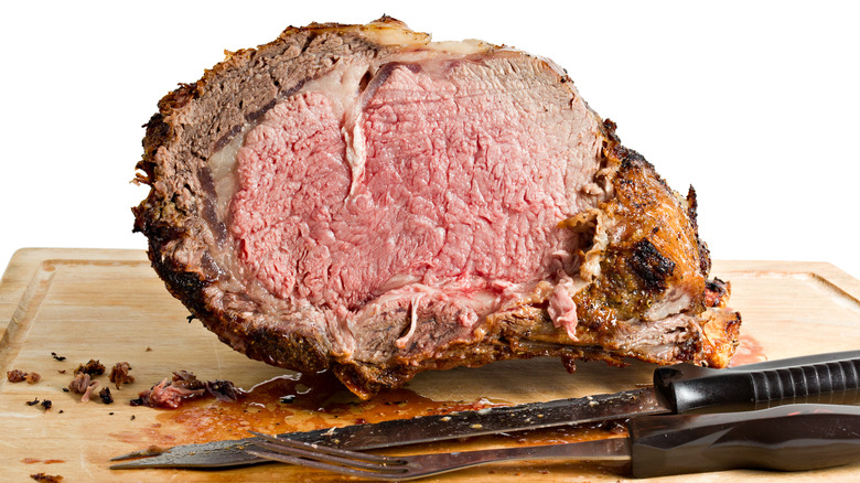 cooked prime rib on cutting board with utensils