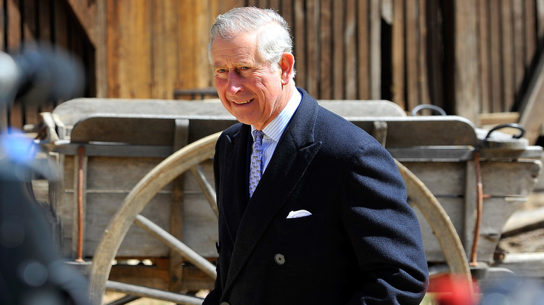 King Charles walking past old fashioned wagon.