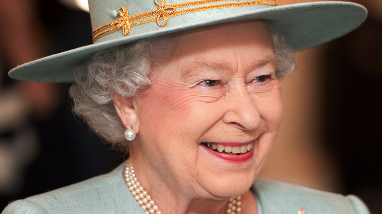 Queen Elizabeth in a blue and gold brimmed hat.