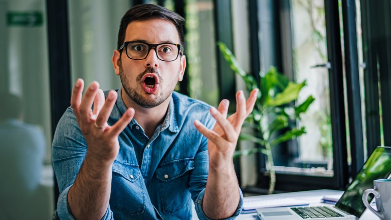 Man sitting at desk gesturing why