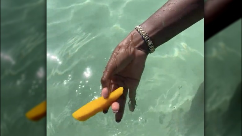 Person dipping mango in ocean