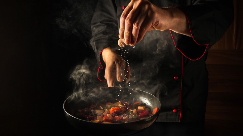 chef salting a pan of vegetables