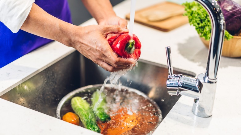 chef washing a bell pepper and other vegetables in a sink