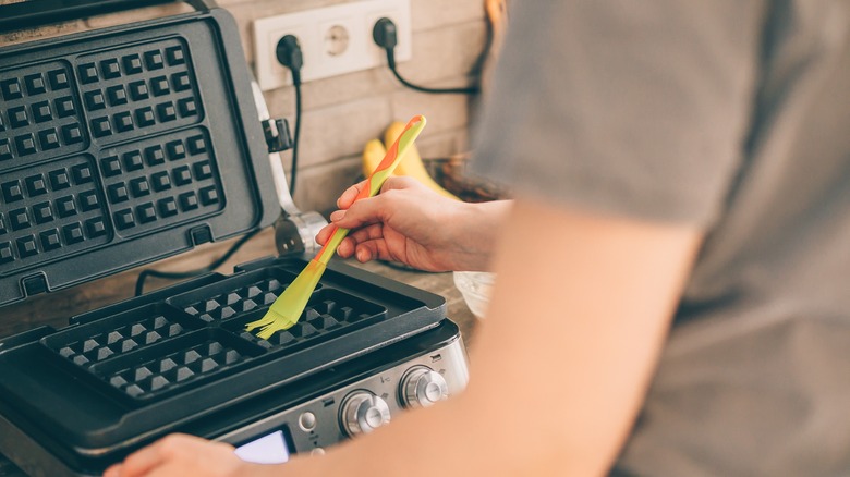 A person greasing a waffle iron