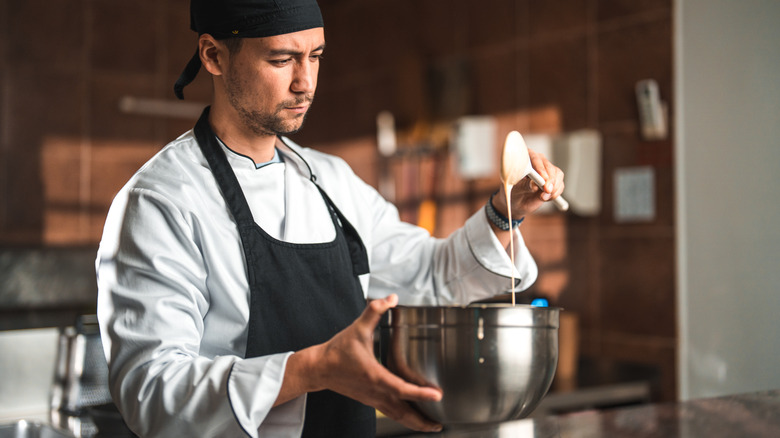 A chef mixing batter with a spoon and a mixing bowl