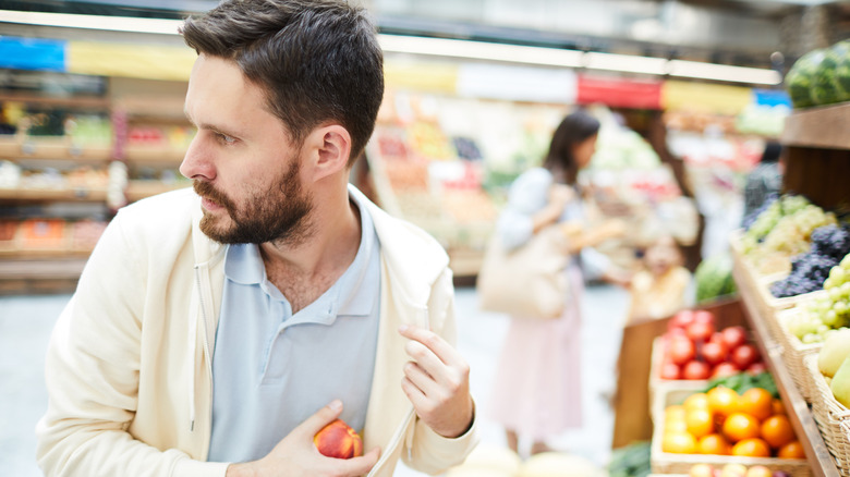 man shoplifting a peach from the grocery store