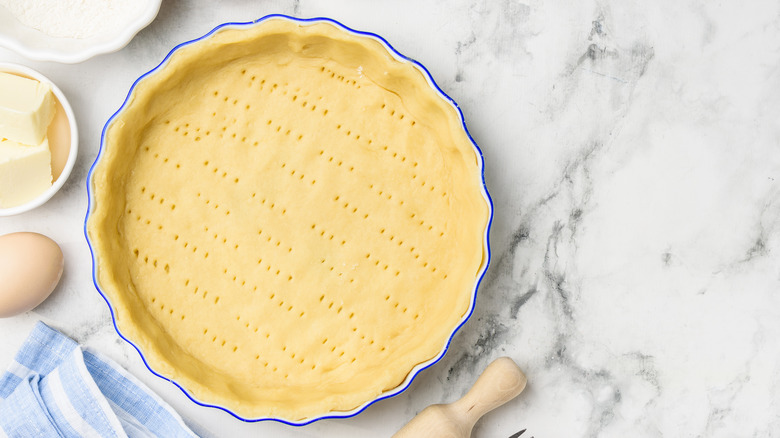 an unbaked pie crust in ceramic plate on a white marble surface