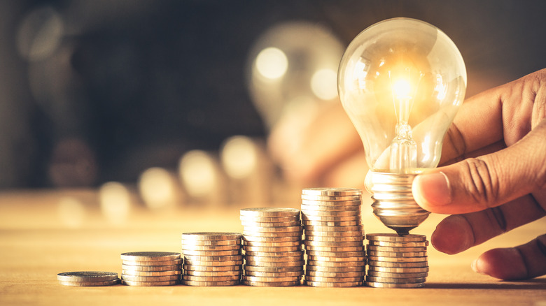 Hand holding light bulb atop stack of coins