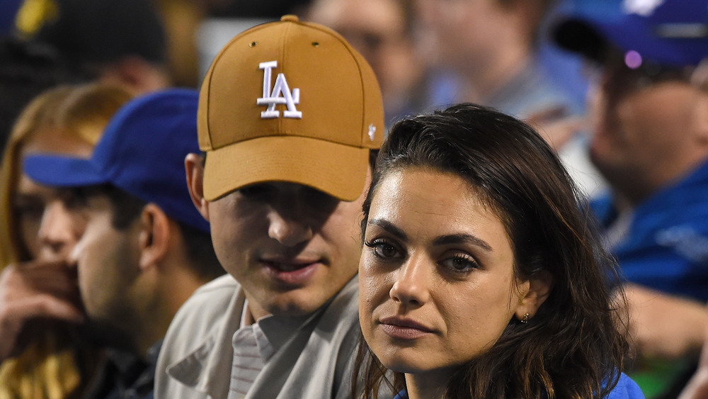 Ashton Kutcher wearing an LA hat and Mila Kunis