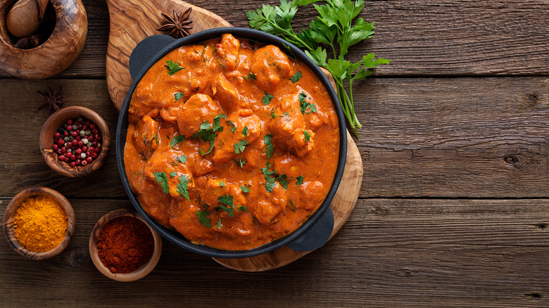 A bowl of butter chicken surrounded by bowls of Indian spices