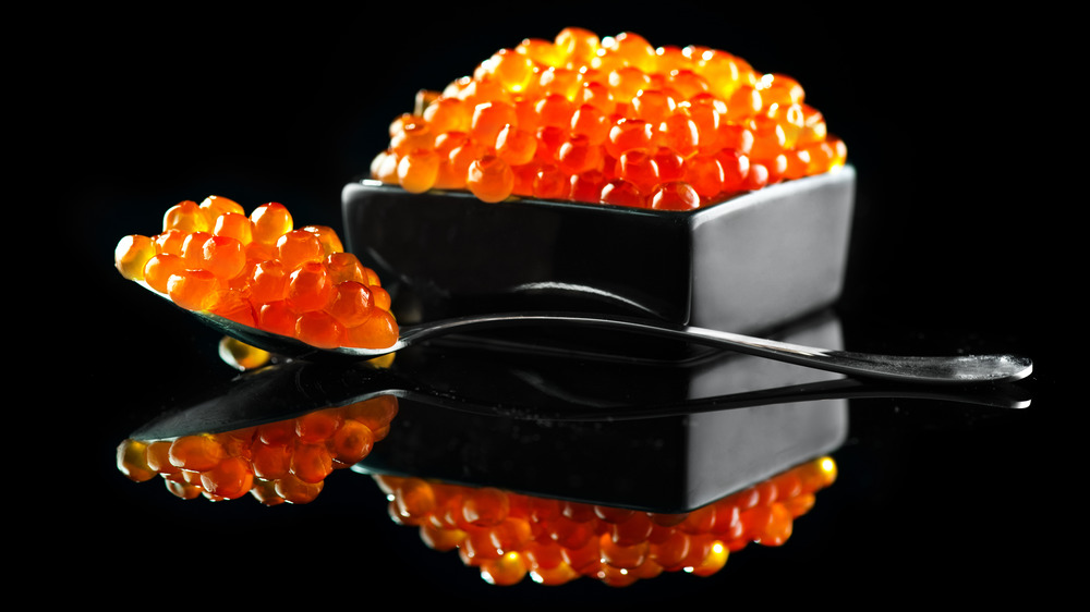 Red caviar in spoon next to bowl of red caviar