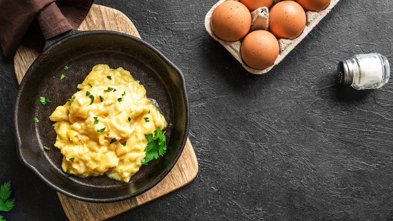 A pan with scrambled eggs next to whole eggs and salt