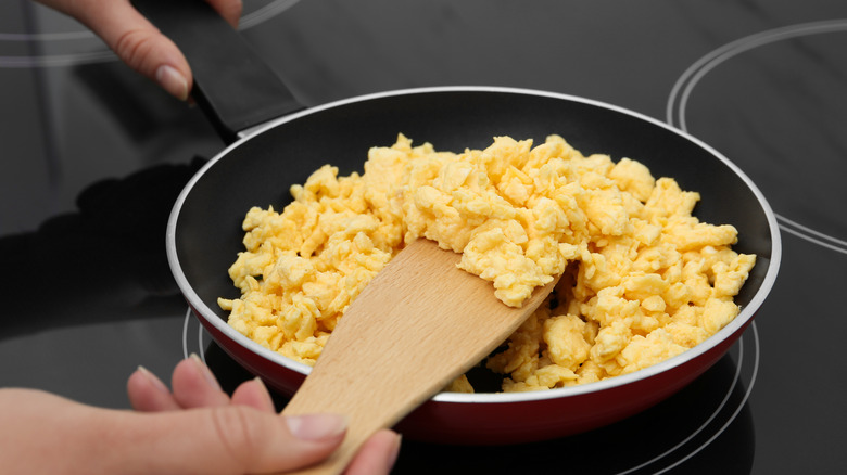 A person sticking a wooden spatula into a pan of scrambled eggs